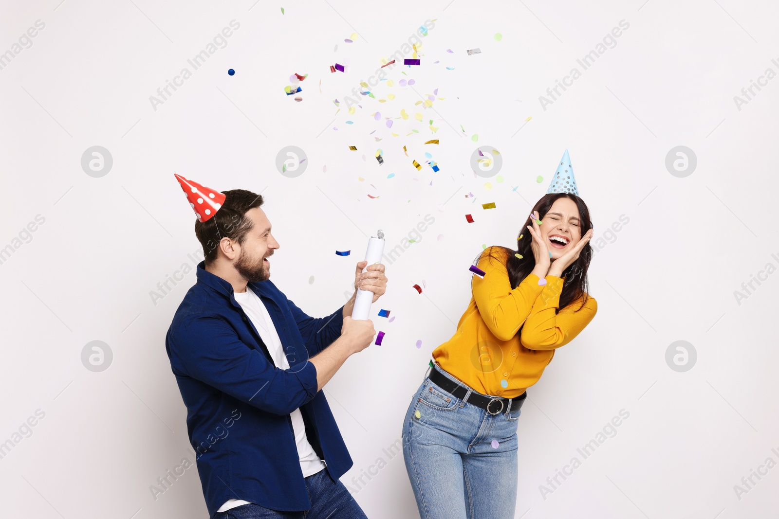 Photo of Happy friends blowing up confetti popper on white background. Surprise party