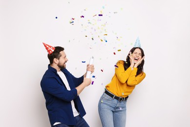 Photo of Happy friends blowing up confetti popper on white background. Surprise party