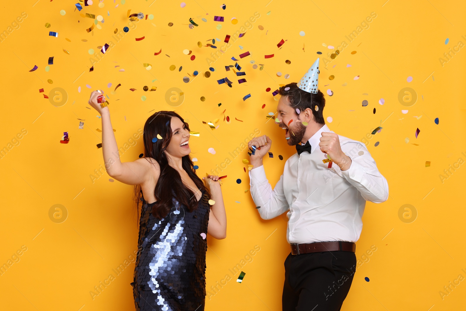 Photo of Happy friends having fun under flying confetti on orange background. Surprise party