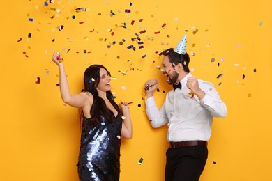 Photo of Happy friends having fun under flying confetti on orange background. Surprise party