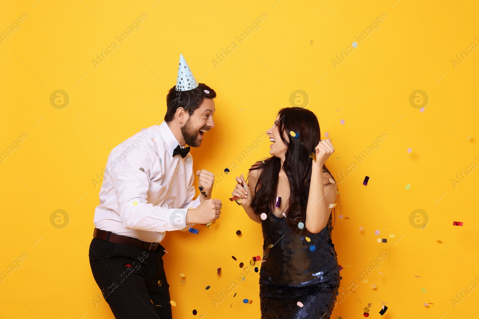 Photo of Happy friends having fun and flying confetti on orange background. Surprise party