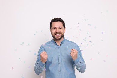 Photo of Happy man and falling confetti on white background. Surprise party