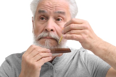 Photo of Senior man with comb applying oil onto his beard on white background