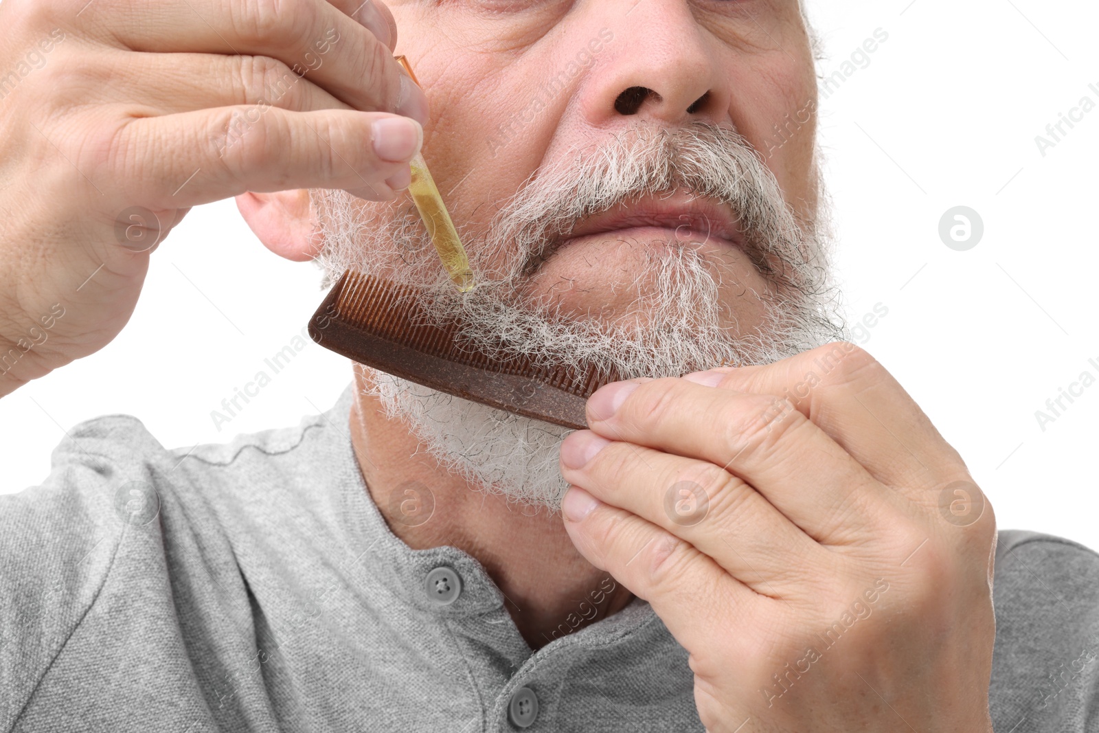 Photo of Senior man with comb applying oil onto his beard on white background, closeup