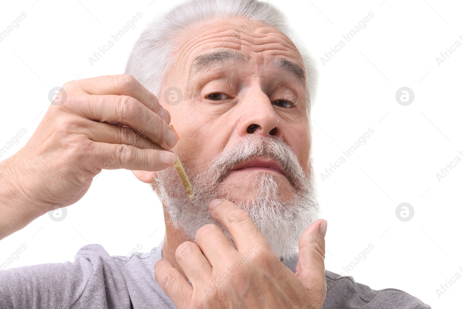 Photo of Senior man applying oil onto his beard on white background