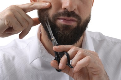 Photo of Man trimming beard with scissors on white background, closeup