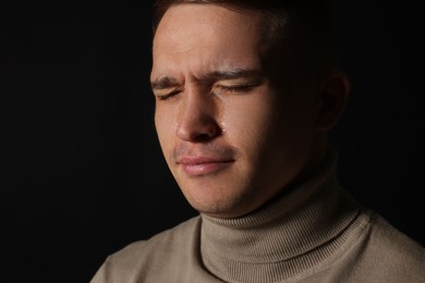 Photo of Distressed young man crying on black background