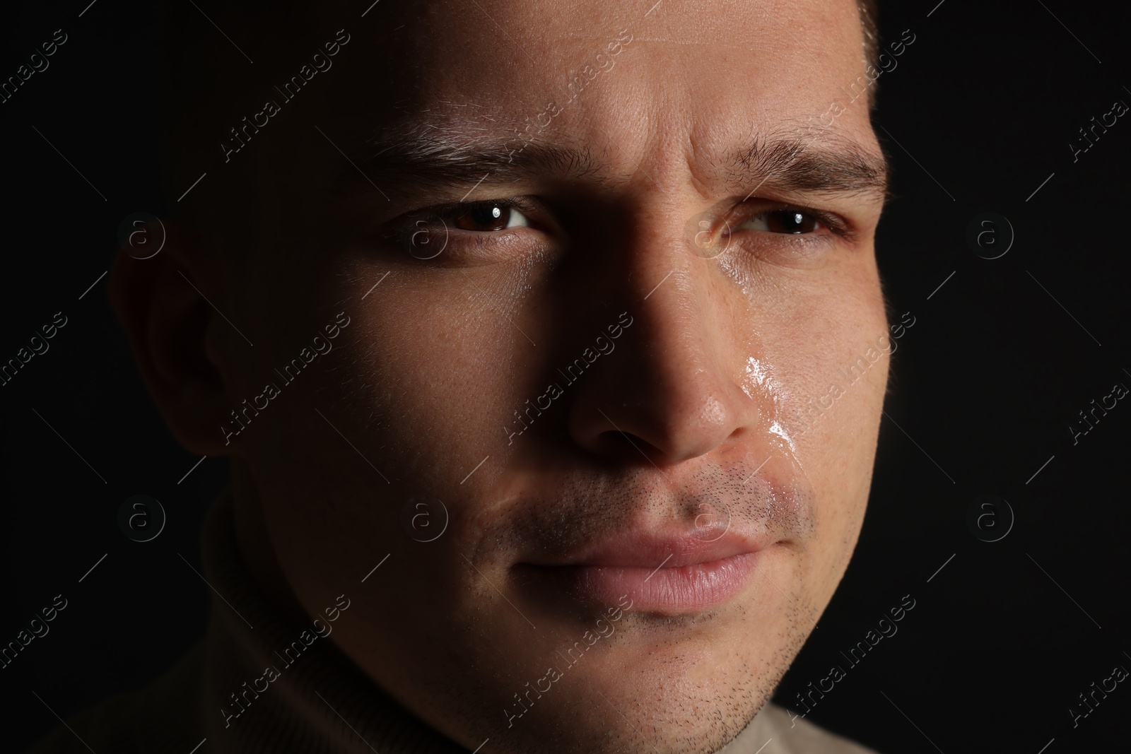 Photo of Distressed young man crying on black background, closeup