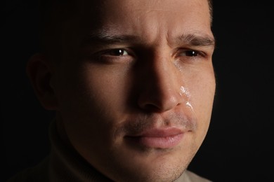 Distressed young man crying on black background, closeup