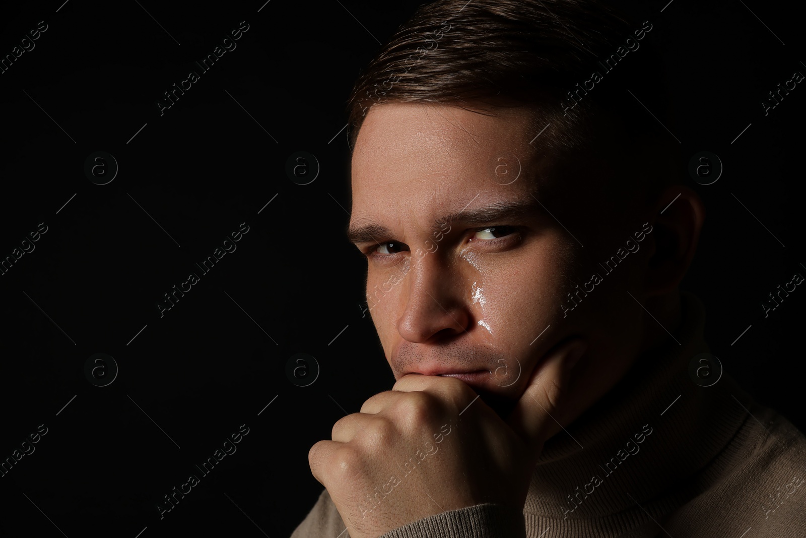 Photo of Distressed young man crying on black background. Space for text