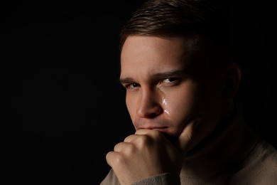 Distressed young man crying on black background. Space for text