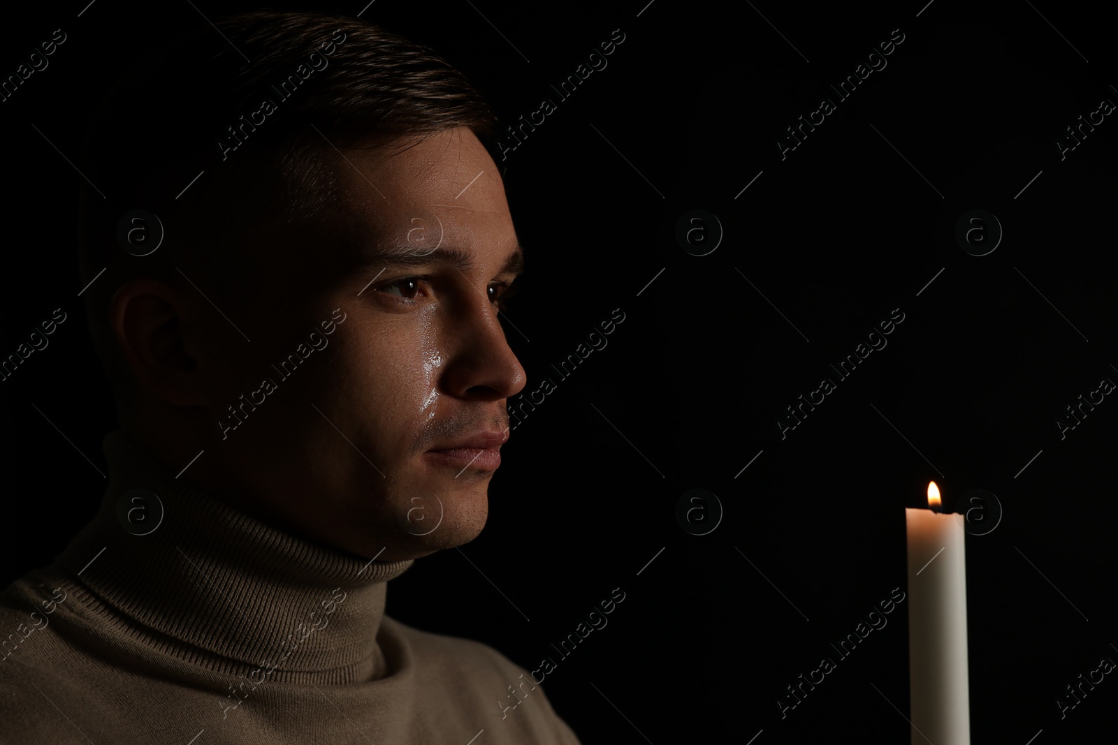 Photo of Man with burning candle crying on black background. Space for text