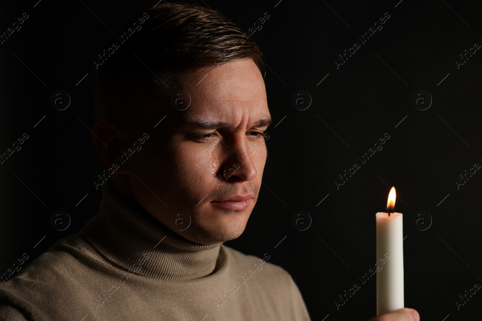 Photo of Man with burning candle crying on black background. Space for text