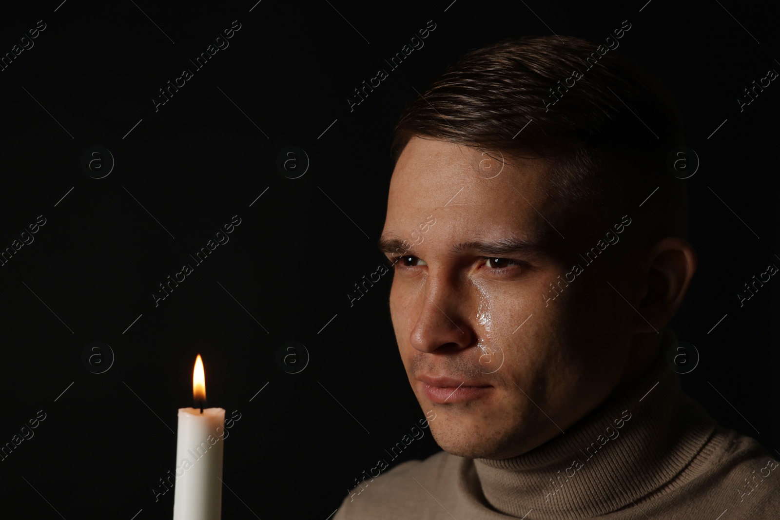 Photo of Man with burning candle crying on black background. Space for text