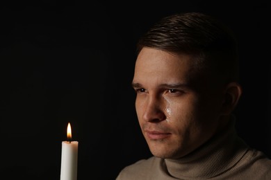 Photo of Man with burning candle crying on black background. Space for text