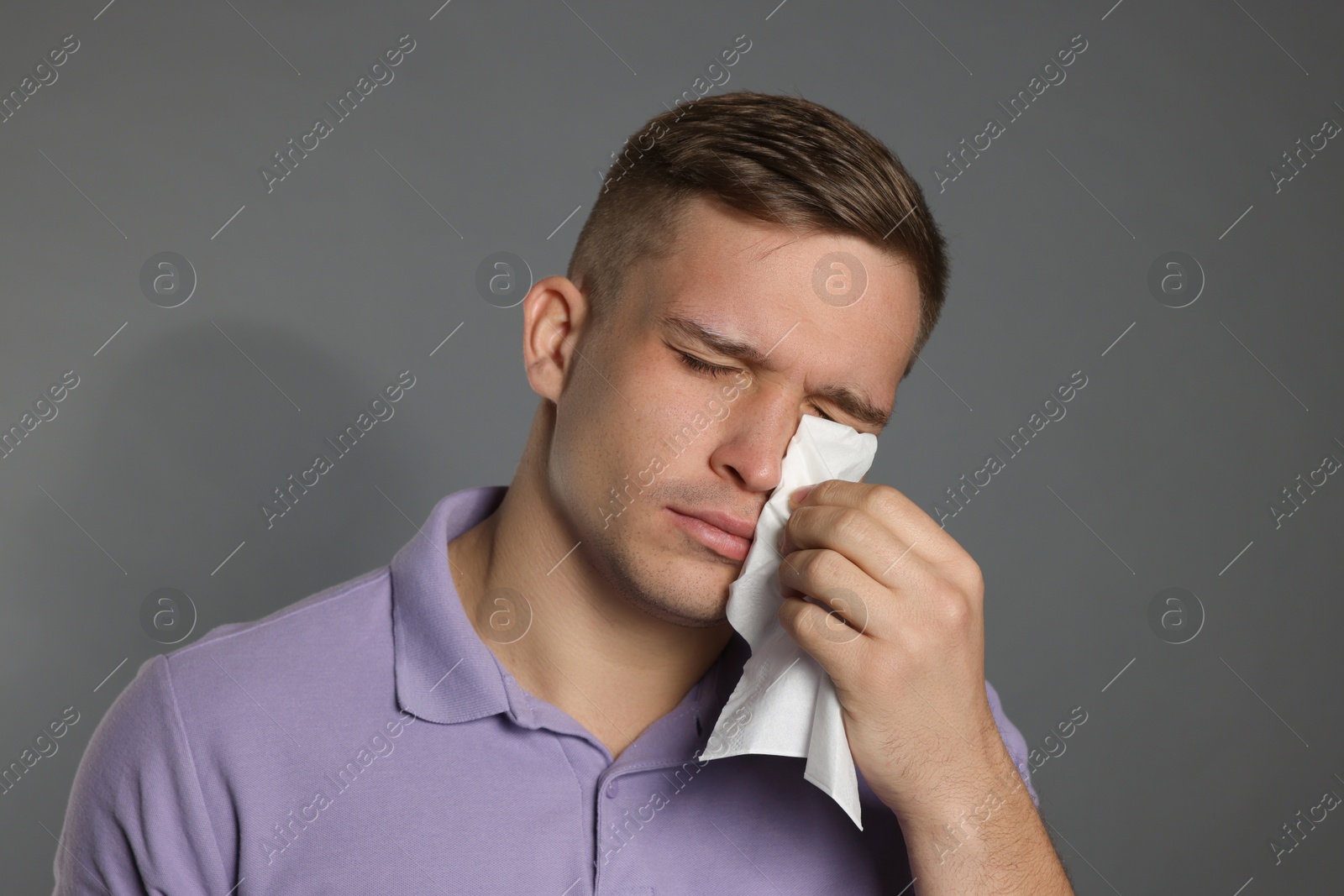 Photo of Crying man wiping tears with tissue on grey background