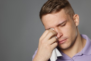 Photo of Crying man wiping tears with tissue on grey background. Space for text