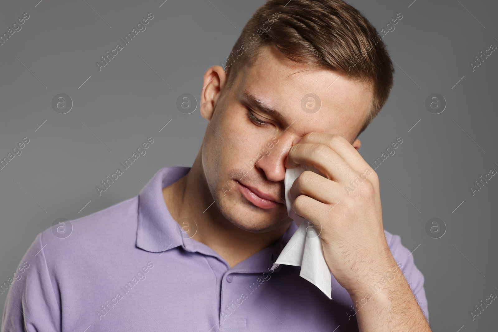 Photo of Crying man wiping tears with tissue on grey background