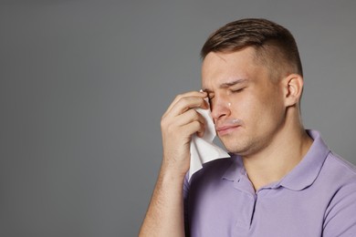 Photo of Crying man wiping tears with tissue on grey background. Space for text