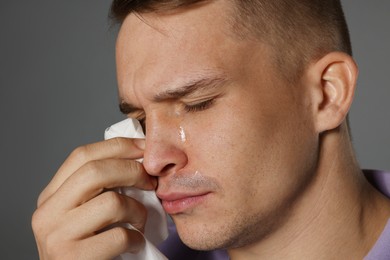 Photo of Crying man wiping tears with tissue on grey background, closeup