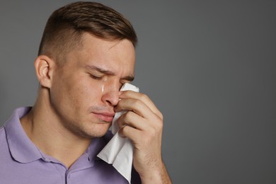 Photo of Crying man wiping tears with tissue on grey background. Space for text