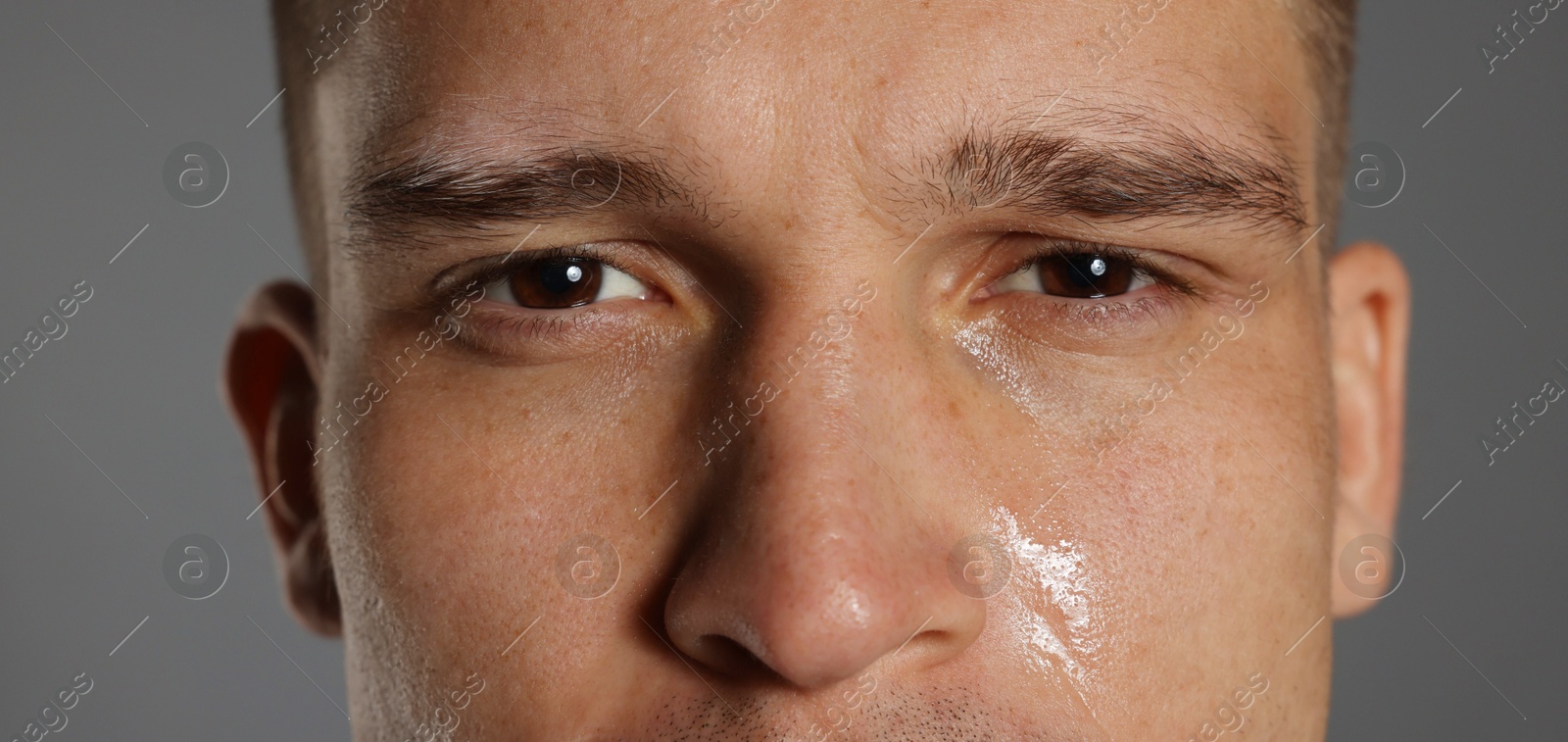 Photo of Distressed young man crying on grey background, closeup