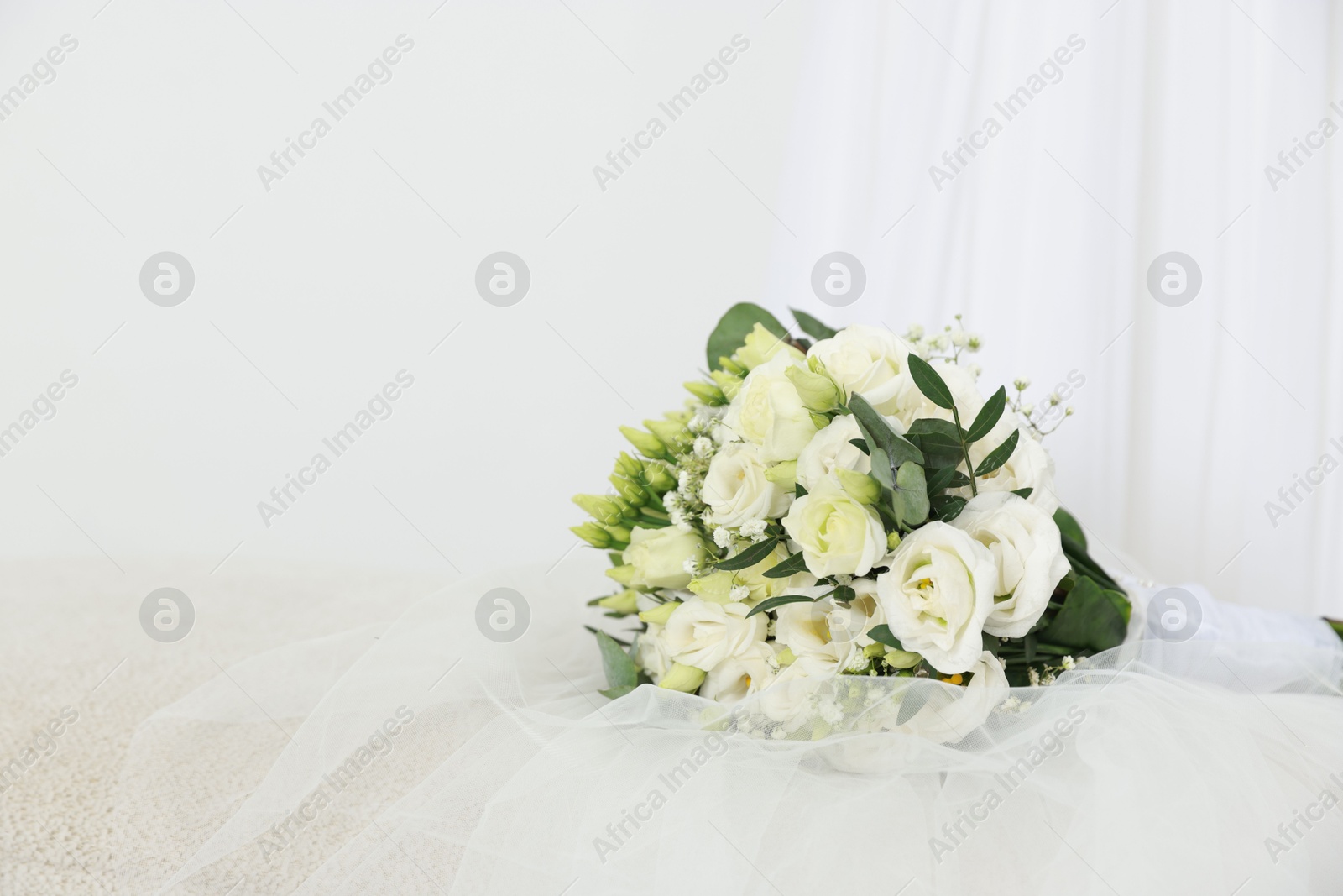 Photo of Beautiful wedding bouquet and veil on pouf against light background, space for text