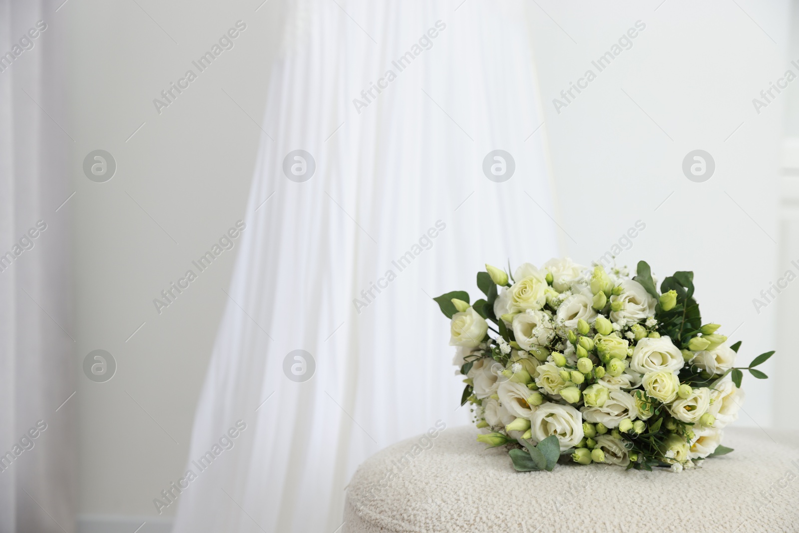 Photo of Beautiful wedding bouquet on pouf and dress against light background