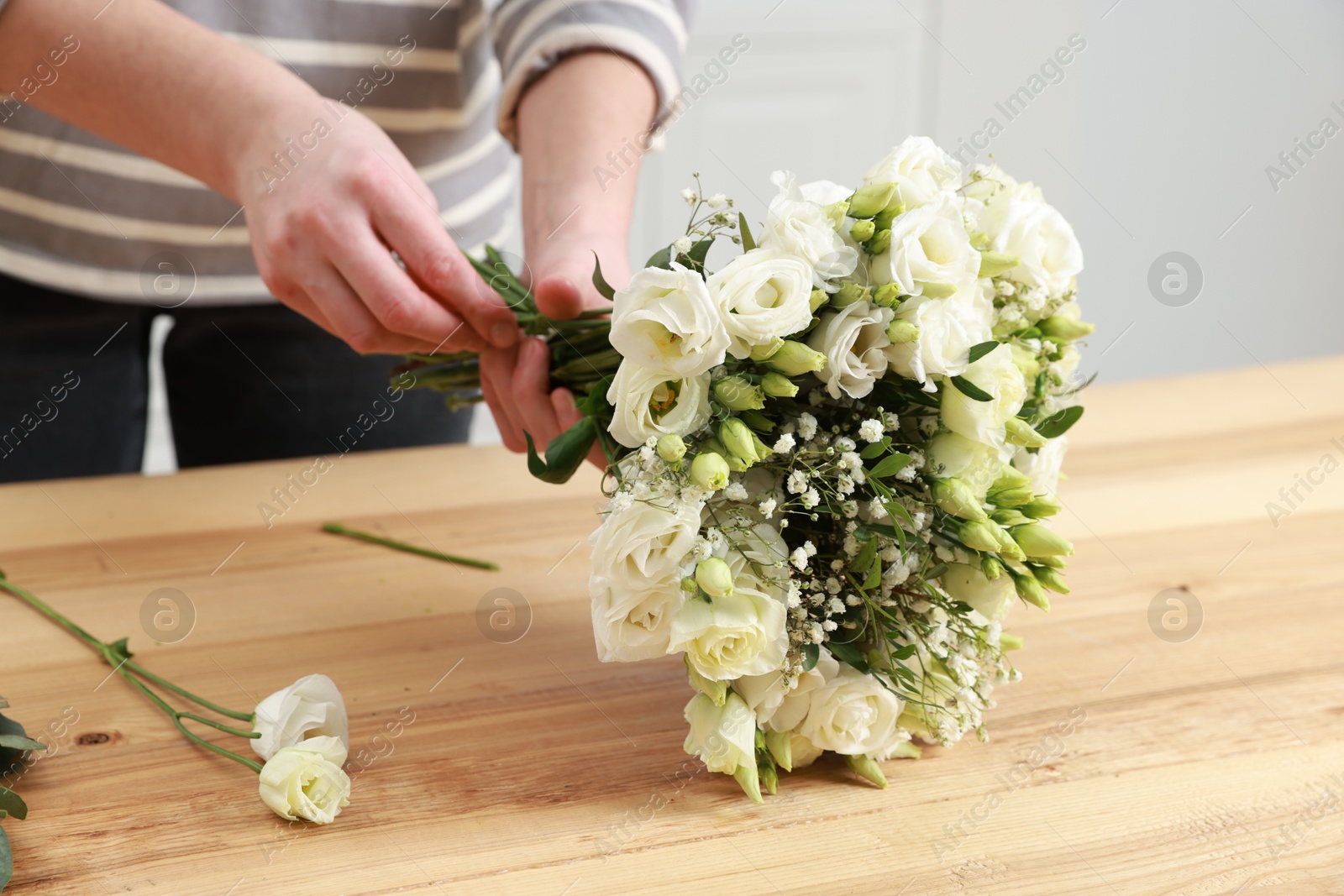 Photo of Florist making beautiful wedding bouquet at wooden table indoors, closeup