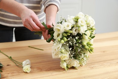 Photo of Florist making beautiful wedding bouquet at wooden table indoors, closeup