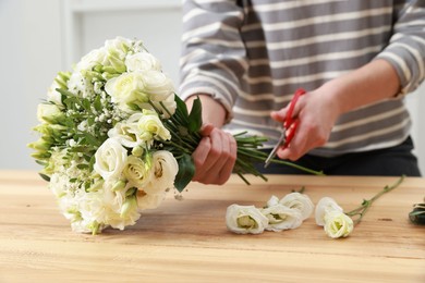 Photo of Florist making beautiful wedding bouquet at wooden table indoors, closeup