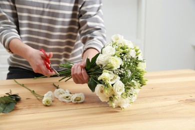 Photo of Florist making beautiful wedding bouquet at wooden table indoors, closeup