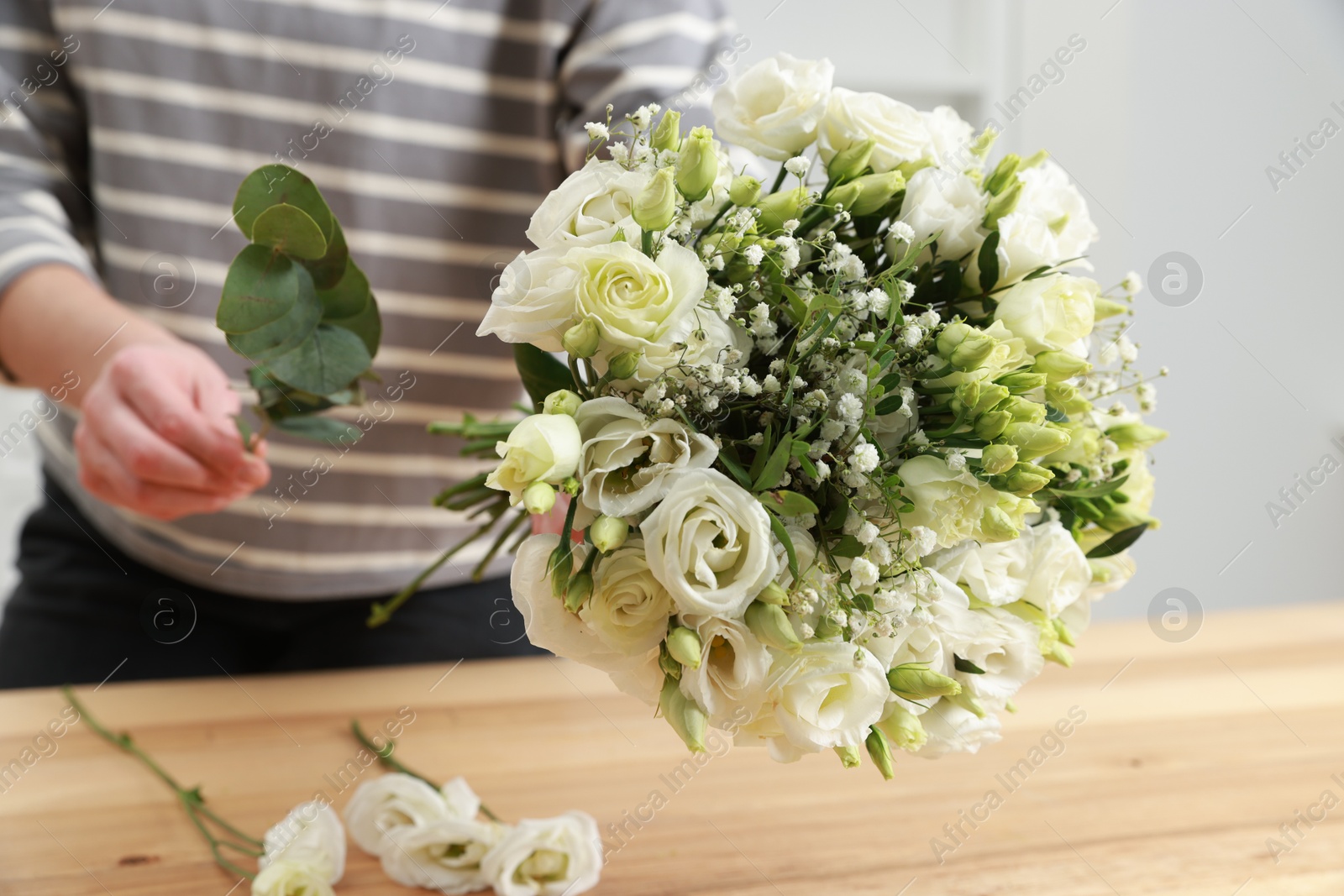 Photo of Florist making beautiful wedding bouquet at wooden table indoors, closeup