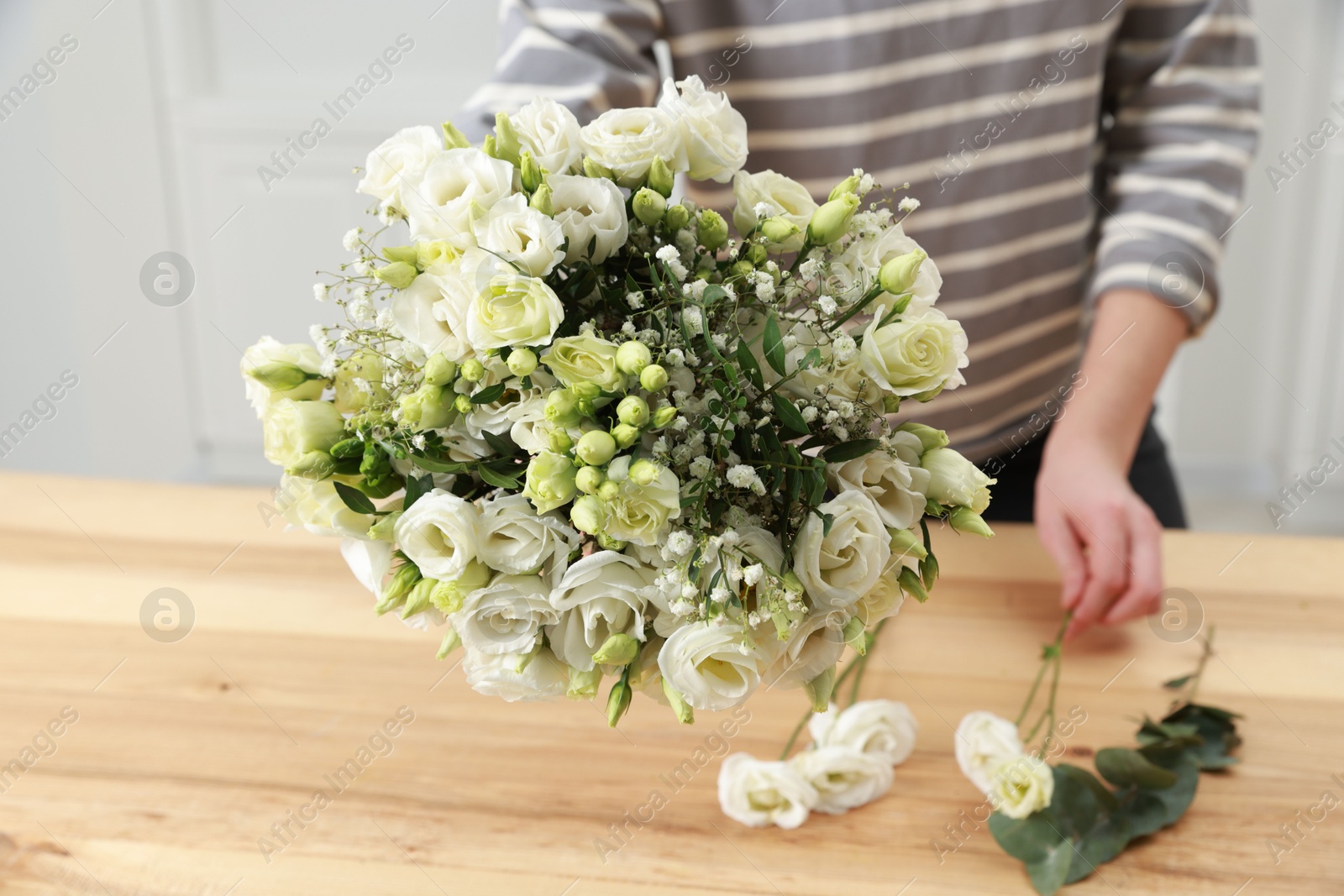 Photo of Florist making beautiful wedding bouquet at wooden table indoors, closeup