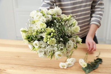 Photo of Florist making beautiful wedding bouquet at wooden table indoors, closeup