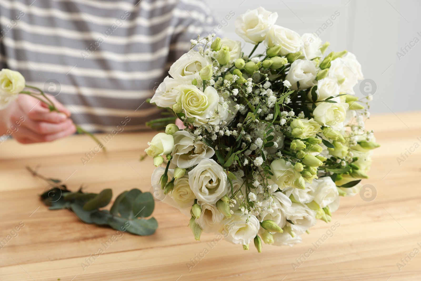 Photo of Florist making beautiful wedding bouquet at wooden table indoors, closeup