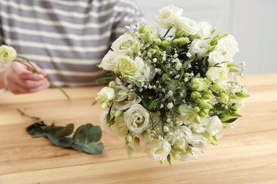 Photo of Florist making beautiful wedding bouquet at wooden table indoors, closeup