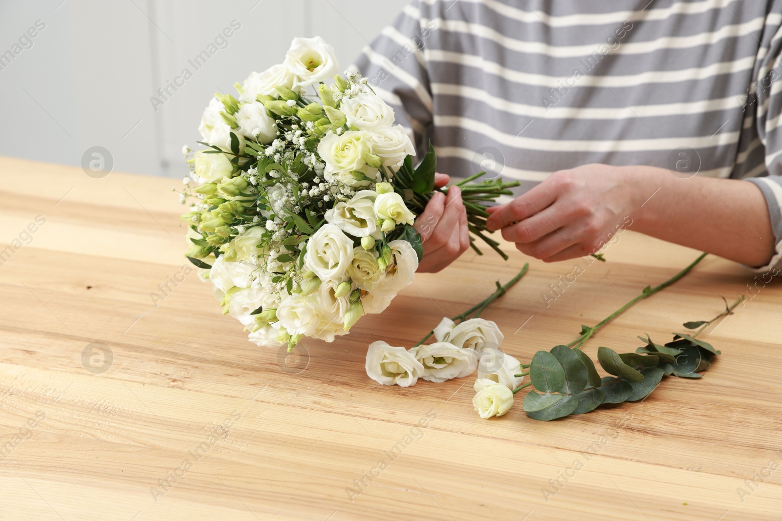 Photo of Florist making beautiful wedding bouquet at wooden table indoors, closeup