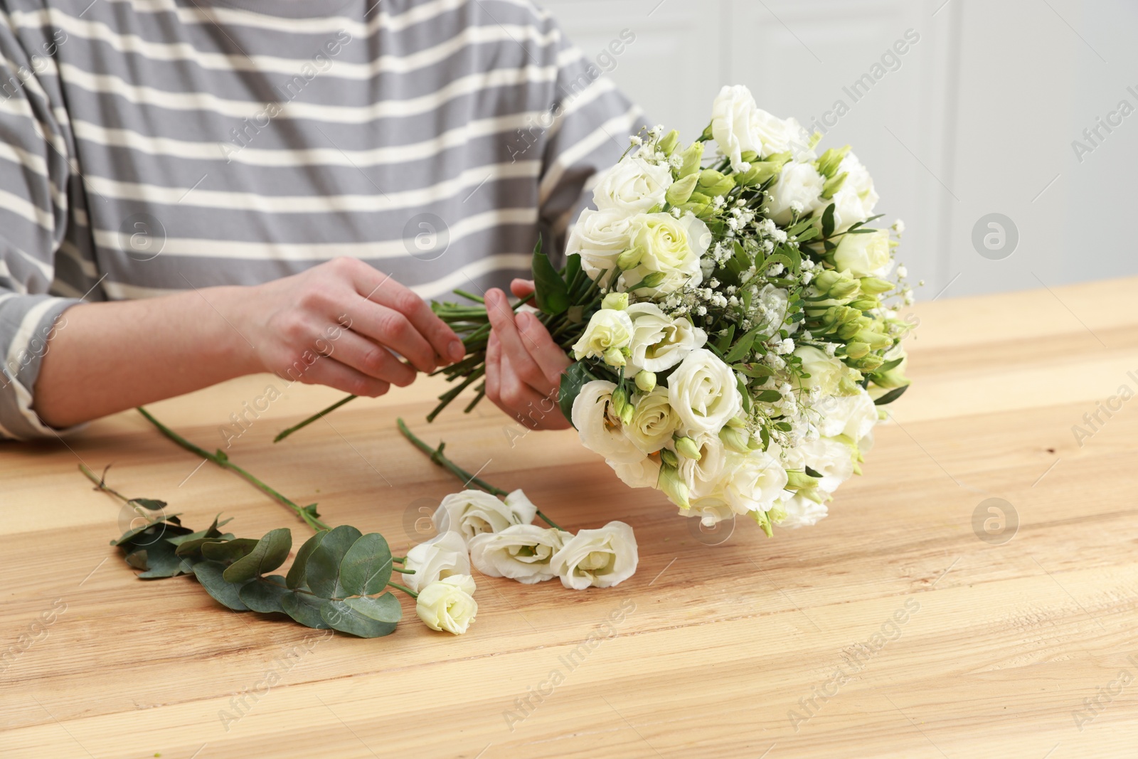 Photo of Florist making beautiful wedding bouquet at wooden table indoors, closeup