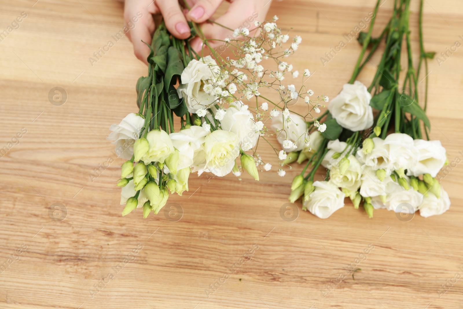 Photo of Florist making beautiful wedding bouquet at wooden table, top view