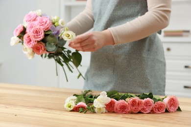 Photo of Florist making beautiful wedding bouquet at wooden table indoors, closeup