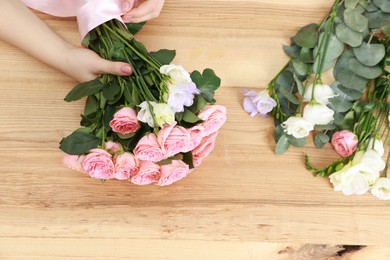 Photo of Florist making beautiful wedding bouquet at wooden table, top view