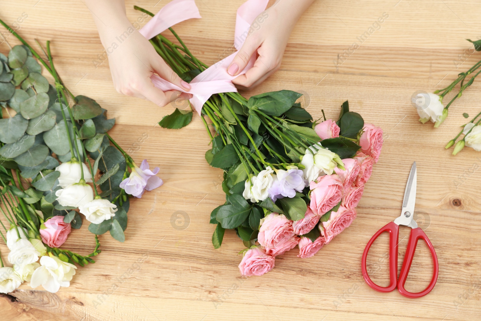 Photo of Florist making beautiful wedding bouquet at wooden table, top view