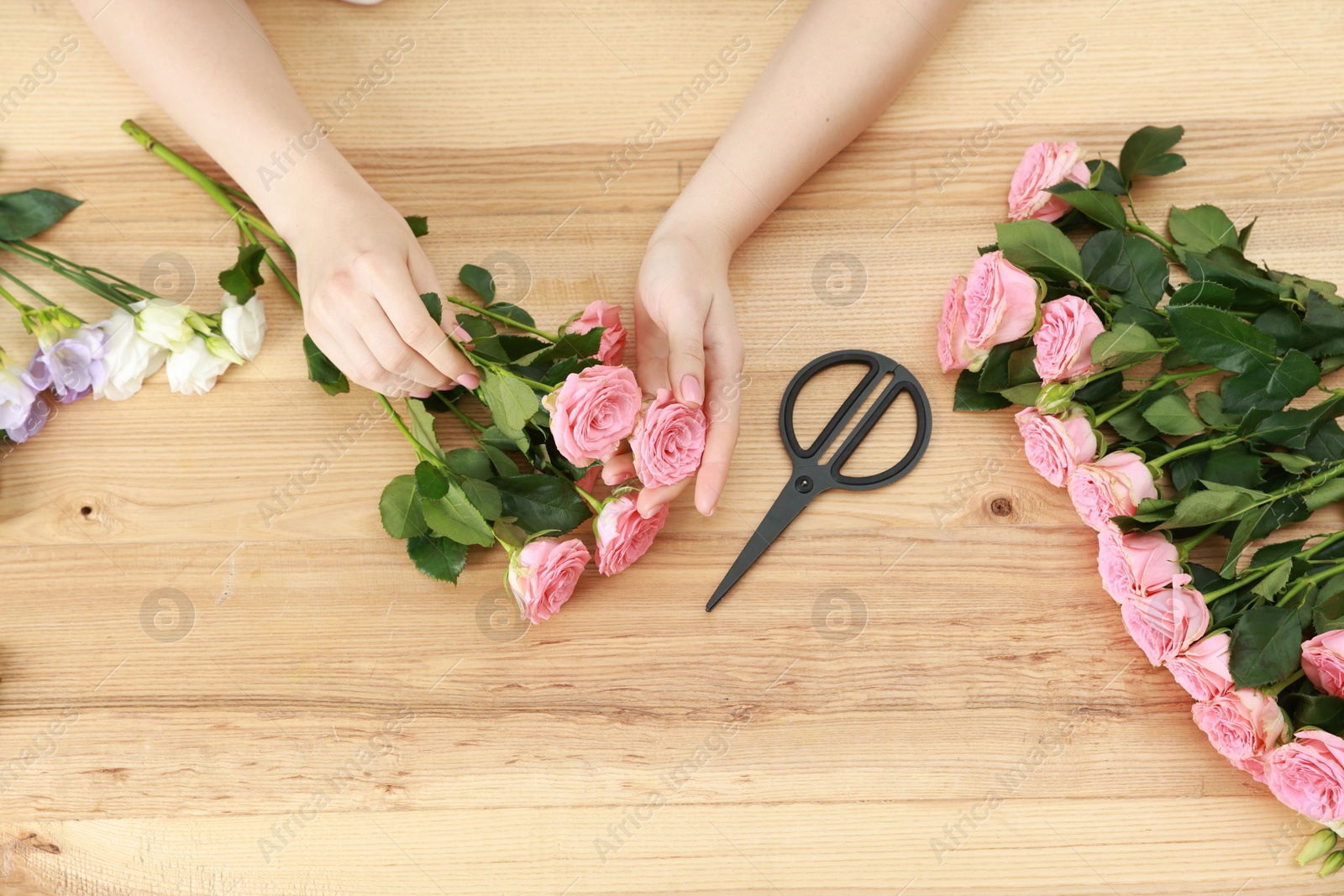 Photo of Florist making beautiful wedding bouquet of fresh rose flowers at wooden table, top view