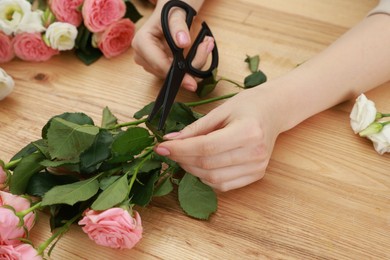 Photo of Florist making beautiful wedding bouquet of fresh rose flowers at wooden table, closeup