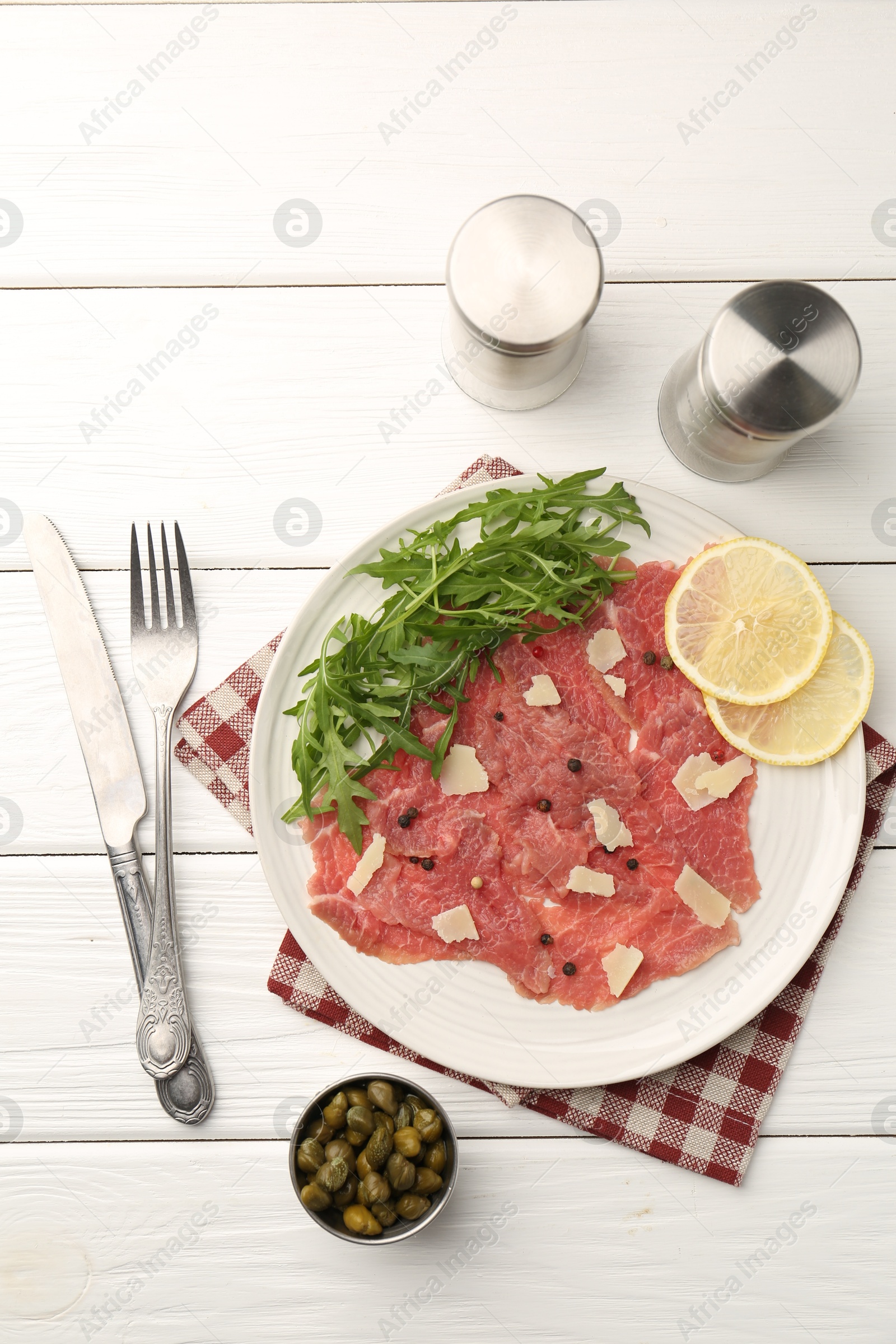 Photo of Fresh beef carpaccio with arugula, lemon and cheese served on white wooden table, flat lay