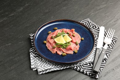 Photo of Fresh beef carpaccio with arugula, lemon and capers on dark textured table