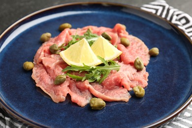 Fresh beef carpaccio with arugula, lemon and capers on plate, closeup