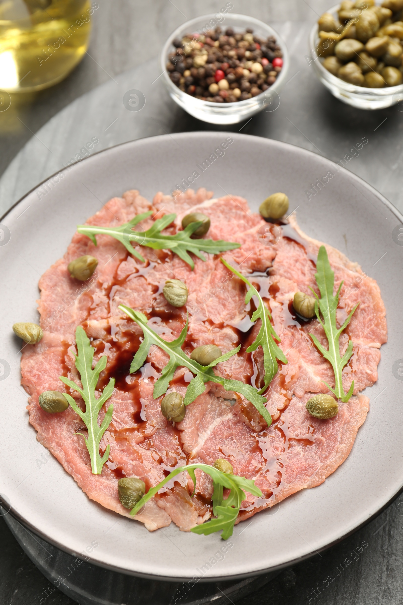 Photo of Fresh beef carpaccio with arugula, capers and sauce on dark textured table, above view