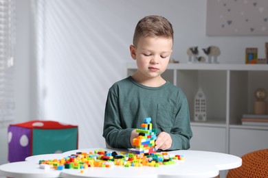 Photo of Cute boy playing with building blocks at white table indoors